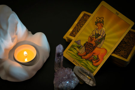 Gold embossed tarot cards, candle in a plaster candlestick and natural crystals on the table. The Major Arcana card Strength lies facing the viewer. high quality photoの写真素材