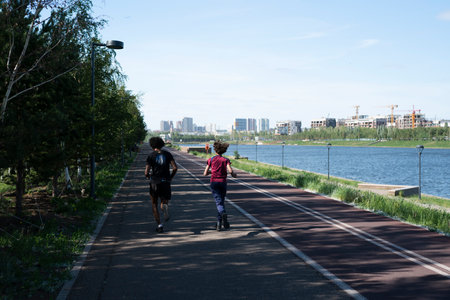 Nur-Sultan, Kazakhstan, June 25, 2022. A dark-skinned guy and a girl with an African hairstyle run along the promenade in the street.のeditorial素材