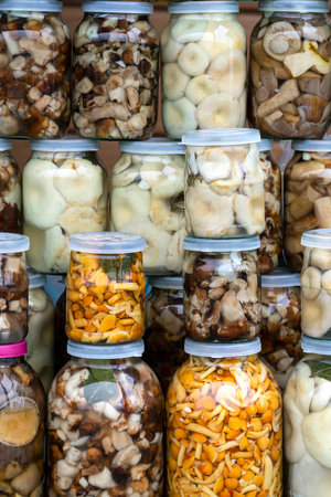 Pickled mushrooms (chanterelles, milk mushrooms, porcini mushrooms) in jars on the counter. small home business. own production. high quality photoの写真素材
