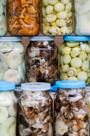 Pickled mushrooms (chanterelles, milk mushrooms, porcini mushrooms) in jars on the counter. small home business. own production. high quality photoの写真素材
