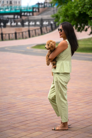 A beautiful Asian girl (Kazakh) holds a dog (mini poodle) in her hands. The girl has emotions of happiness and joy on her face. high quality photoの写真素材