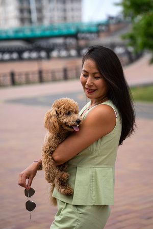 A beautiful Asian girl (Kazakh) holds a dog (mini poodle) in her hands. The girl has emotions of happiness and joy on her face. high quality photoの写真素材