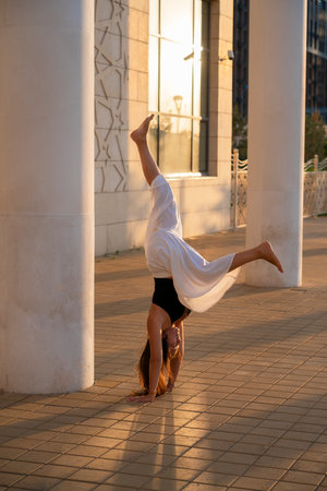 Young Asian woman practicing yoga outdoors during daytime with the view of the city. The girl performs a handstand at the column. Urban yoga, sunrise workout.の写真素材