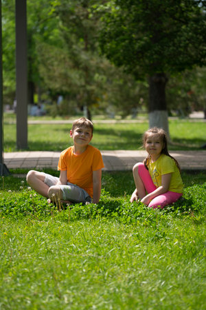 Children boy and girl (brother and sister) are sitting in the grass in the city park. high quality photoの写真素材