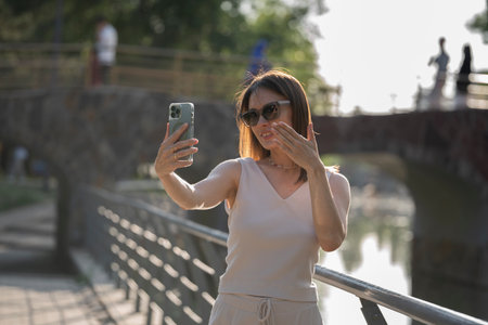 Backlit summer portrait of a young brunette woman in sunglasses. A woman sends an air kiss to an interlocutor on a video call. high quality photoの写真素材