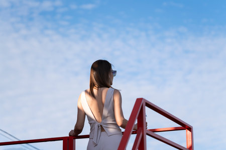 Summer portrait of young brunette woman against blue sky. A woman with a beautiful back stands with...