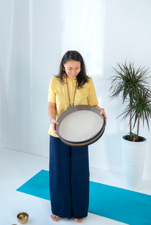 A young asian woman, a brunette with long hair, holds a tambourine (ocean drum) in her hands. high quality photoの写真素材