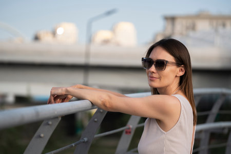 Summer urban portrait of a young brunette woman in sunglasses. The portrait was taken during the golden hour under backlight. high quality photoの写真素材
