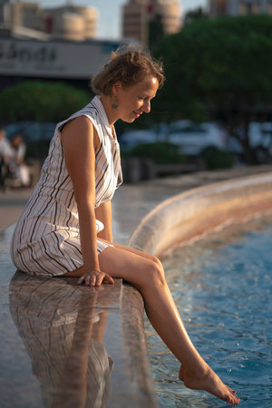 Portrait of a young blonde woman who sits at the city fountain. high quality photoの写真素材