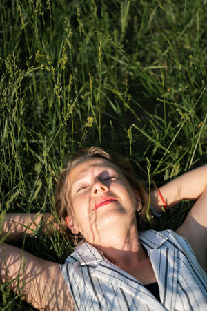 Young blond woman lies in the green grass. Carelessness, freedom, dreams, being in the moment. high...