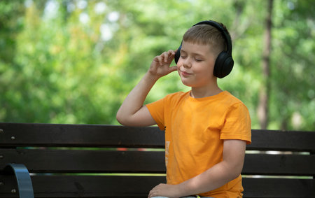 Outdoor portrait of a blond boy of eight years old with wireless headphones on his head. Concept:...