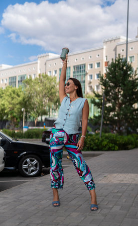 A young Asian woman in sunglasses stands on the street and holds a reusable cup for hot drinks in her hands. high quality photoの写真素材