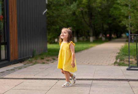A two-year-old girl in a yellow dress walks in the park. high quality photoの写真素材