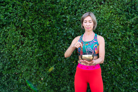 Portrait of a mature woman, 59 years old, who holds a Tibetan singing bowl in her hands on the street against the backdrop of green trees. . high quality photoの写真素材