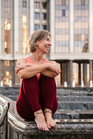 Portrait of a mature woman, 59 years old, sitting by the fountain and resting after yoga practice. Active sport lifestyle of mature people. Sports in the life of a senior woman.の写真素材