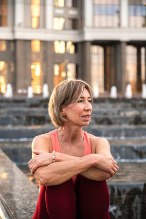 Portrait of a mature woman, 59 years old, sitting by the fountain and resting after yoga practice....
