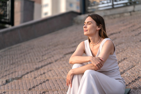 Summer urban portrait of a young woman. A woman sits on the embankment and thinks about something. high quality photoの写真素材