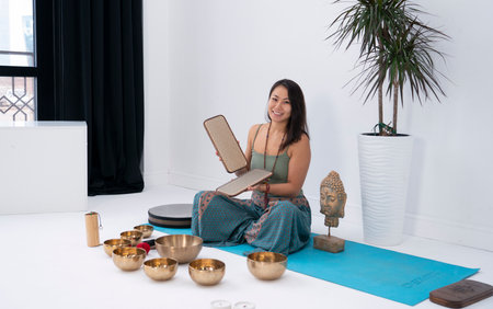 A young Asian woman sits in a lotus position near the Tibetan communal bowls. A woman holds Sadhu boards in her hands. high quality photoの写真素材