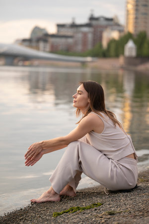 Summer urban portrait of a young brunette woman. The woman sits on the bank of the river and thinks about something. high quality photoの写真素材