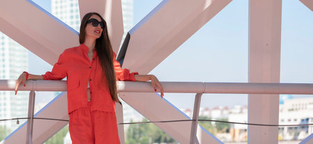 Summer portrait of a girl with long blond hair. A girl in sunglasses and orange clothes stands near the city embankment. High quality photoの写真素材