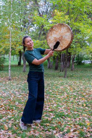 An Asian girl in modern clothes with a shamanic tambourine in her hands. High quality photoの写真素材
