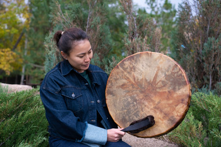 An Asian girl in modern clothes sits on a stone with a shamanic tambourine in her hands. High quality photoの写真素材