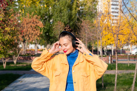 A young woman with headphones on her head listens to music and walks through the autumn park. High quality photoの写真素材