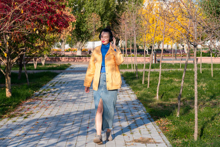 A young woman with headphones on her head listens to music and walks through the autumn park. High quality photoの写真素材