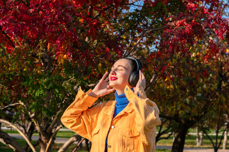 A young woman with headphones on her head listens to music and walks through the autumn park. High quality photoの写真素材