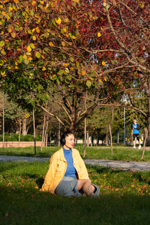 A young woman sits on the green grass in the park and enjoys music on her headphones. High quality photoの写真素材
