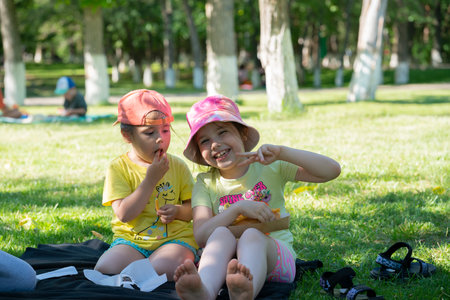Sisters seven and three years old on a picnic. The girls eat while sitting on the grass. High quality photoの写真素材