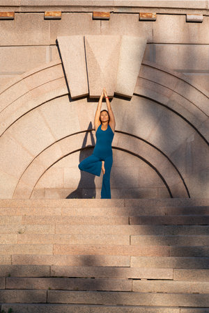 A woman in a blue jumpsuit practices yoga on a city street. High quality photoの写真素材