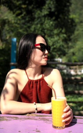 A girl in sunglasses drinks orange juice in a summer cafe. Rishikesh, India. High quality photoの写真素材