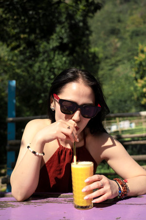 A girl in sunglasses drinks orange juice in a summer cafe. Rishikesh, India. High quality photoの写真素材