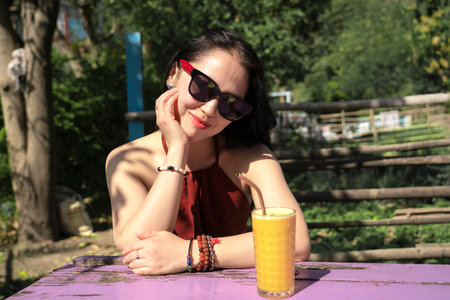 A girl in sunglasses drinks orange juice in a summer cafe. Rishikesh, India. High quality photoの写真素材