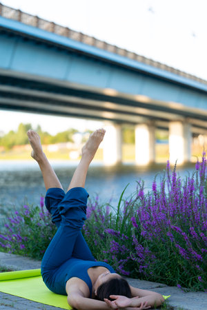 An Asian woman in a blue jumpsuit practices yoga on a city street.の写真素材
