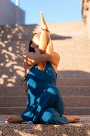 An Asian woman in a blue jumpsuit practices yoga on a city street.