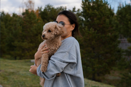 A young Asian woman holds her pet, a toy poodle, in her arms. Autumn walk. High quality photoの写真素材