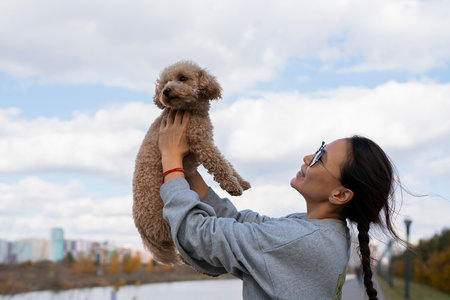 A young Asian woman holds her pet, a toy poodle, in her arms. Autumn walk. High quality photo