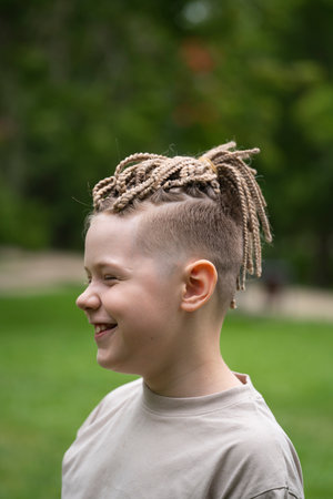 A 10-year-old boy with dreadlocks and African braids on his head. Summer green background. High...