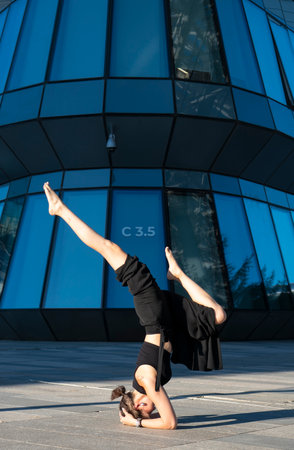 Young Asian woman doing yoga headstand on street in front of building.の写真素材