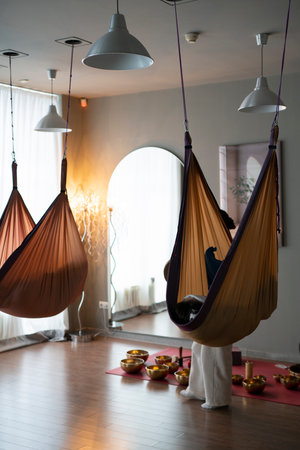 A woman conducts a sound therapy session with singing bowls, people lie in yoga hammocks.の写真素材