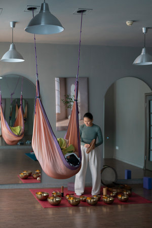 A woman conducts a sound therapy session with singing bowls, people lie in yoga hammocks.の写真素材