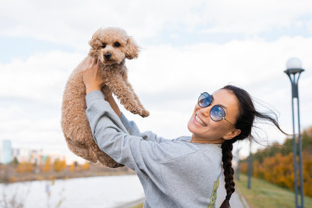 A young Asian woman holds her pet, a toy poodle, in her arms. Autumn walk.の写真素材