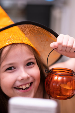 A 10-year-old girl wearing a witchs hat with a pumpkin-shaped candlestick.