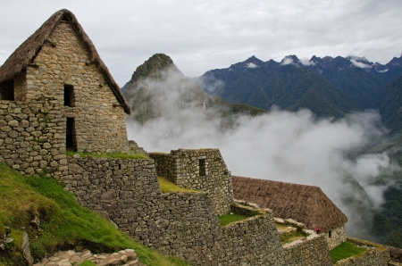 Cabins with thatched roofs at the entrance to the Imca village Machu Picchu with clouds obscuring the the mountains in the backgroundのeditorial素材