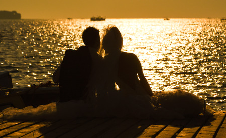 Bride and Groom sitting near the at Sunset. Romantic Married Coupleの写真素材