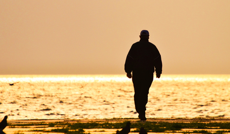 Old man walking alone on the seashore at sunset, silhouette.の写真素材