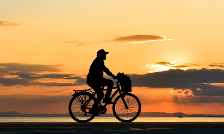 Cyclist man riding bicycle onshore at sunset, silhouette.の写真素材