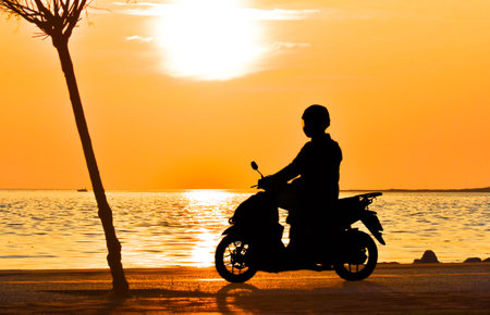 Motorcycle rider riding motorcycle onshore at sunset, silhouette.の写真素材